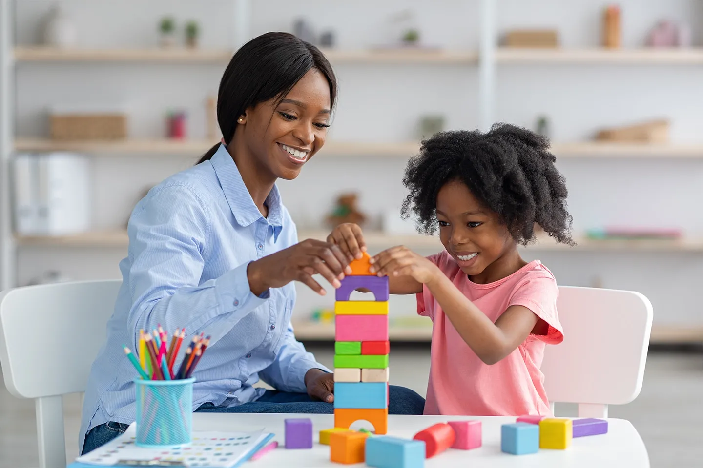 Young black girl and child development specialist playing with building blocks.